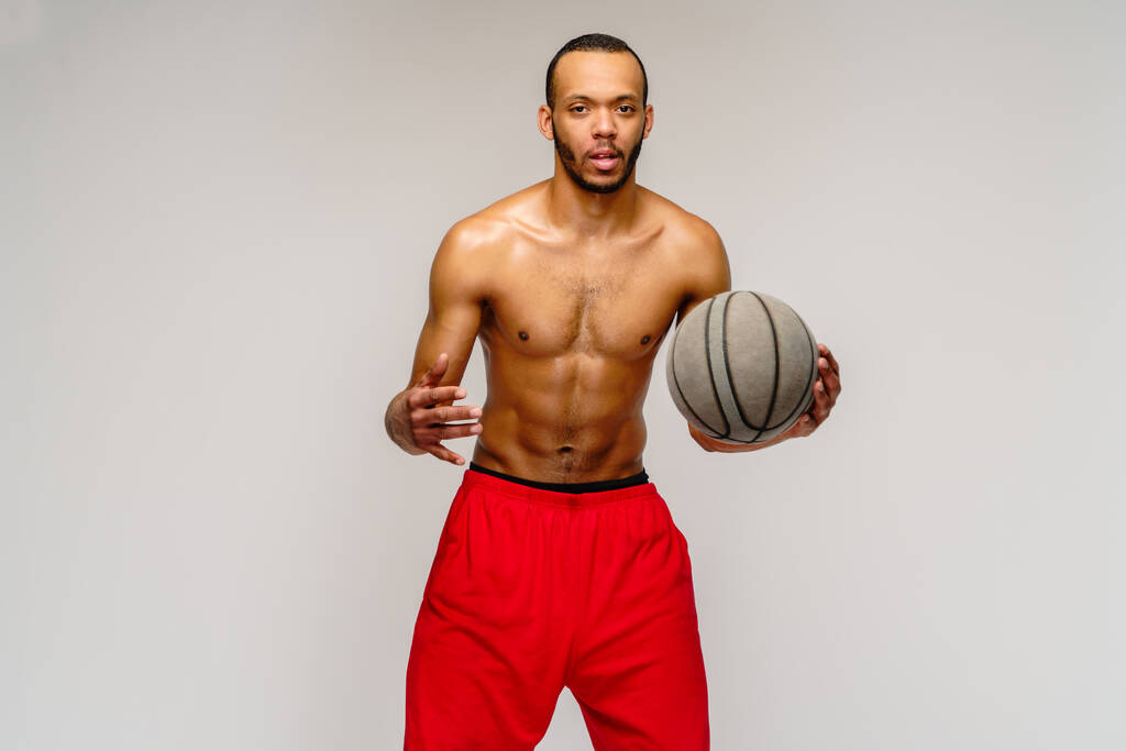 Muscoloso sportivo afroamericano che gioca a basket senza merda su sfondo grigio chiaro - Foto, immagini