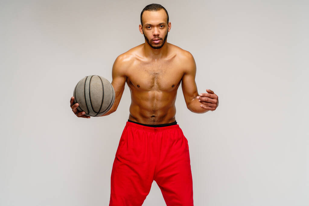 Muscoloso sportivo afroamericano che gioca a basket senza merda su sfondo grigio chiaro - Foto, immagini