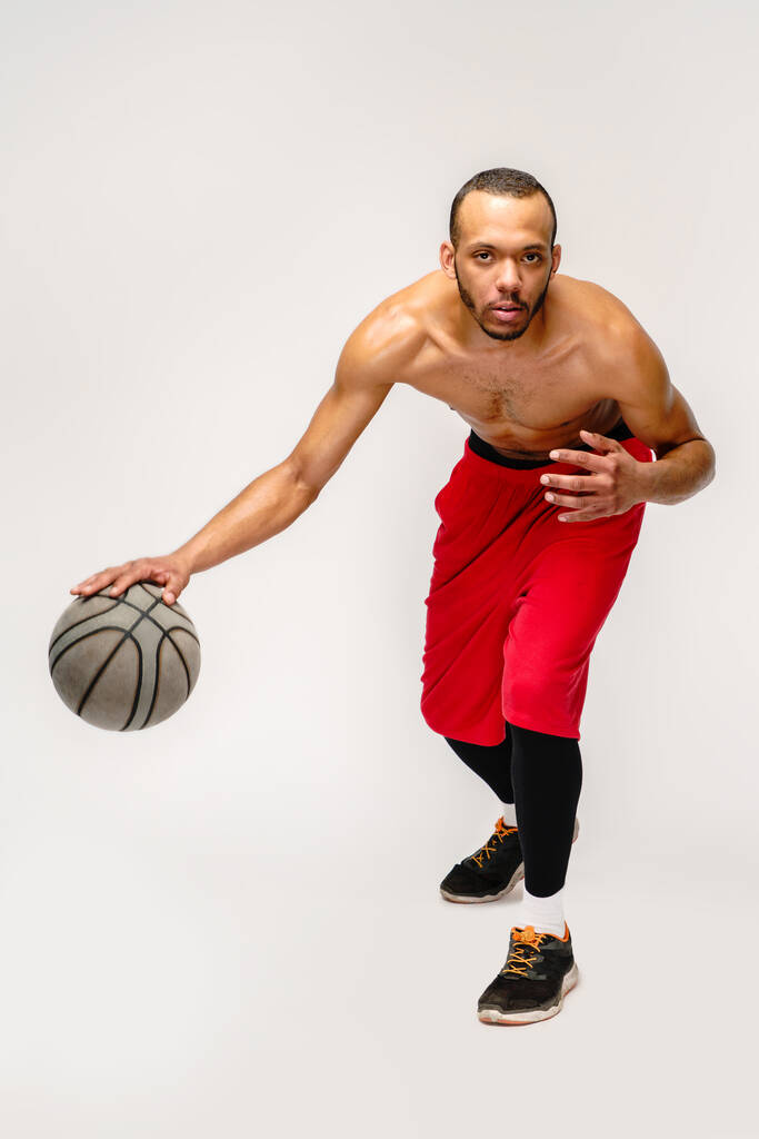 Izmos afro-amerikai sportoló kosárlabda szarul játszik világosszürke háttér - Fotó, kép