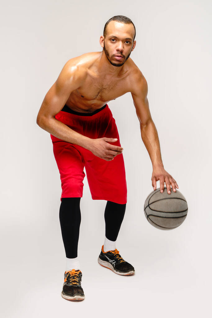 gespierd afrikaanse amerikaanse sportman spelen basketbal poep over licht grijze achtergrond - Foto, afbeelding