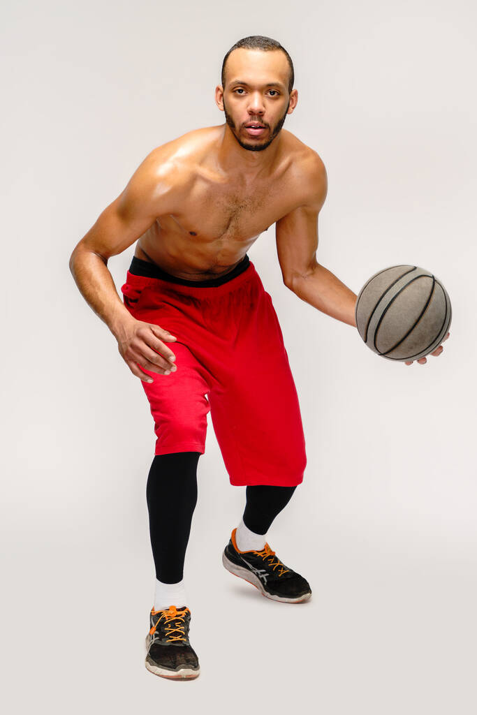 Мускулистый американский спортсмен, играющий в баскетбол на светло-сером фоне - Фото, изображение