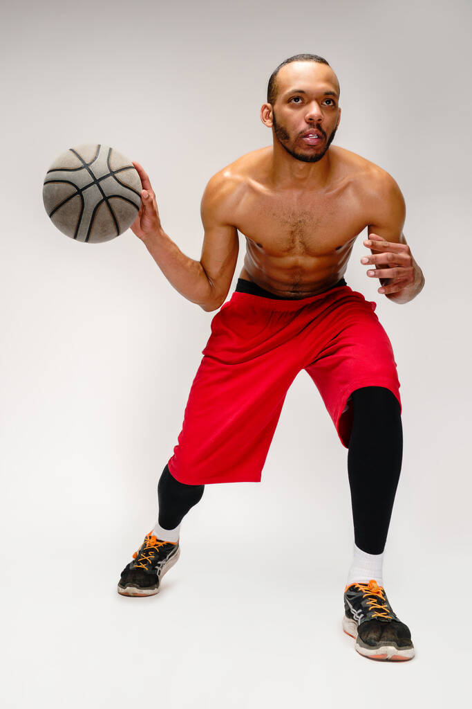 gespierd afrikaanse amerikaanse sportman spelen basketbal poep over licht grijze achtergrond - Foto, afbeelding