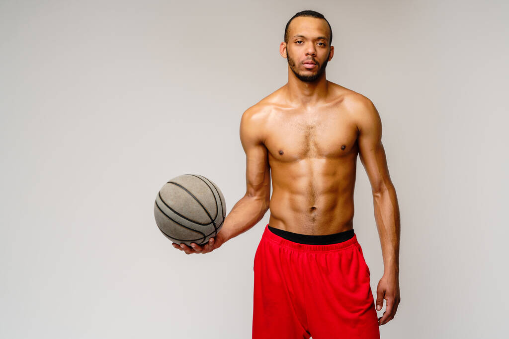 Мускулистый американский спортсмен, играющий в баскетбол на светло-сером фоне - Фото, изображение