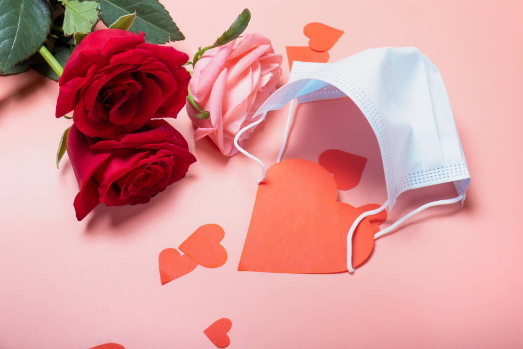 Roses sur un fond rose et un masque médical avec une carte pour la Saint Valentin.. Fond créatif pour la Saint Valentin. - Photo, image