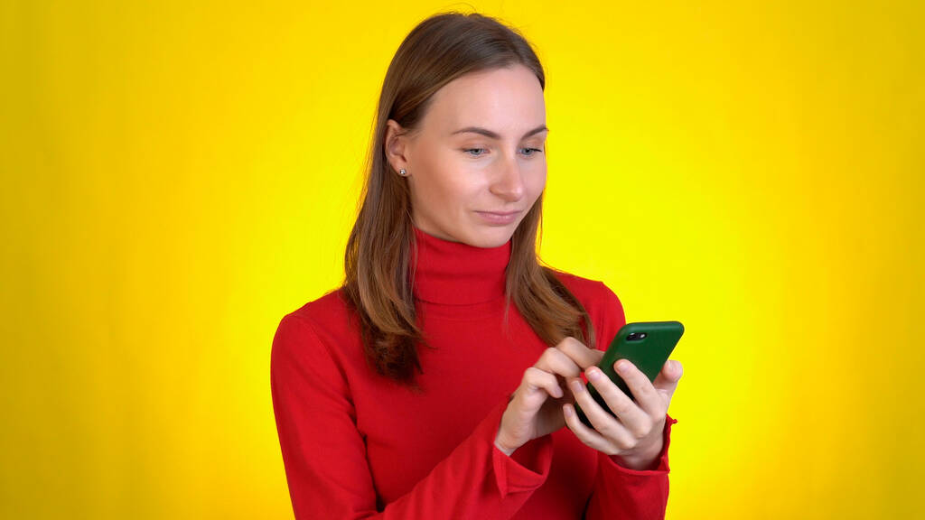 Αστεία νεαρή γυναίκα που ποζάρει απομονωμένη στο κίτρινο στούντιο. Η έννοια του τρόπου ζωής. Χρησιμοποιώντας κινητό τηλέφωνο πληκτρολογώντας sms περιήγηση μήνυμα πω wow καλύπτει το στόμα με ανοιχτό - Φωτογραφία, εικόνα