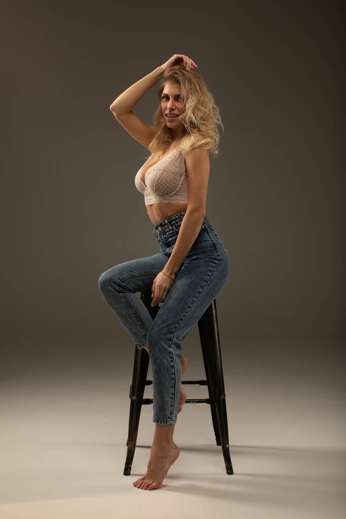 приваблива молода блондинка в мереживо бежевий бюстгальтер і стильні джинси позує в студії
 - Фото, зображення