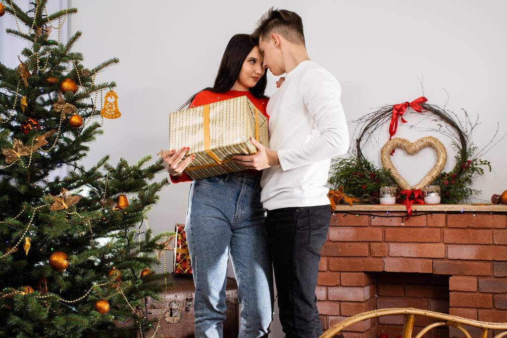婚約者はクリスマスの日に彼の最愛の人に贈り物を与えます。ユニークなクリスマスの雰囲気。休暇中の驚き. - 写真・画像