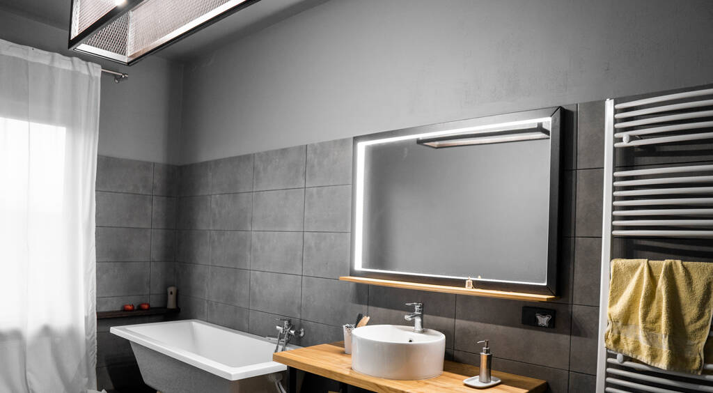 Bathroom in a concrete style with a bath, sink and big mirror. - Fotó, kép