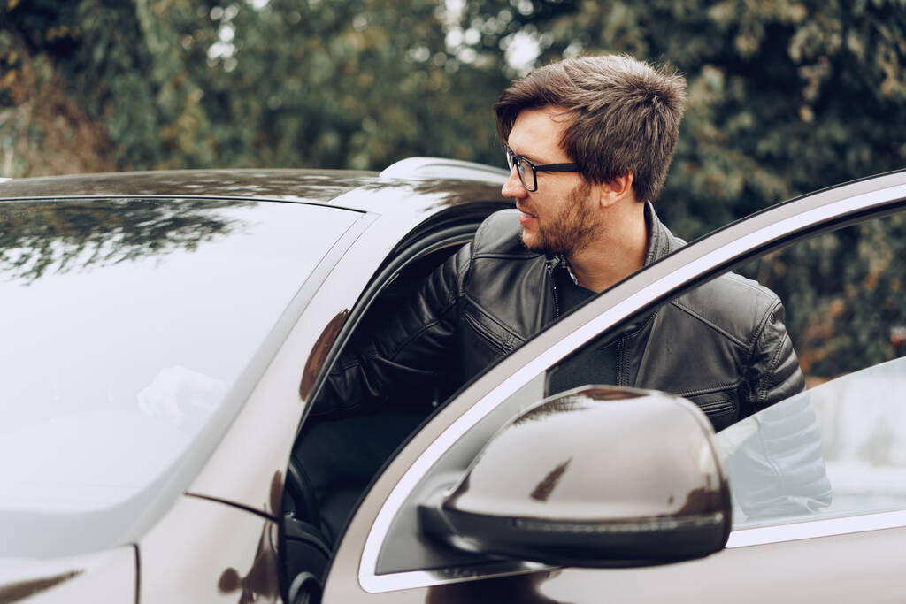 Κομψός άντρας με γυαλιά κάθεται σε ένα αυτοκίνητο. - Φωτογραφία, εικόνα
