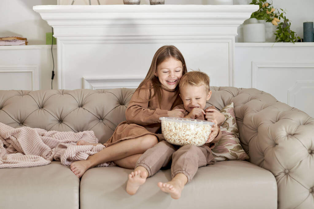 Брат і сестра їдять попкорн, сидячи вдома на дивані. Хлопчик і дівчинка розслабляються розваги і дивитися фільм по телевізору
 - Фото, зображення