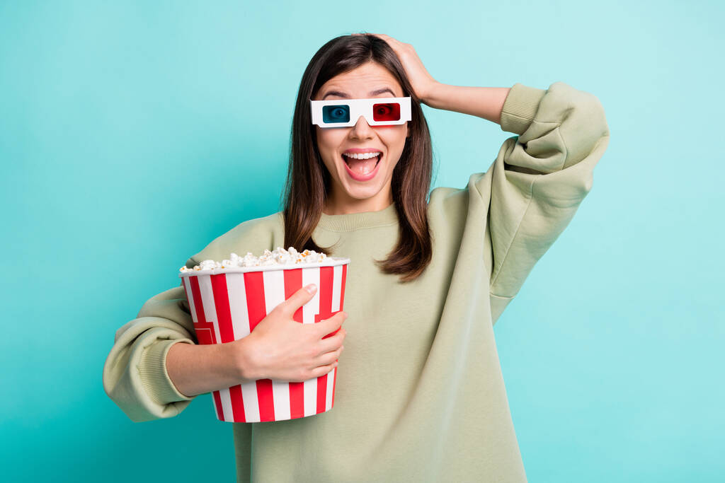Fotoporträt einer schockierten Frau in 3D-Brille, die den Kopf berührt und einen riesigen Popcorn-Eimer in der einen Hand hält, isoliert auf lebendigem kristallfarbenem Hintergrund - Foto, Bild