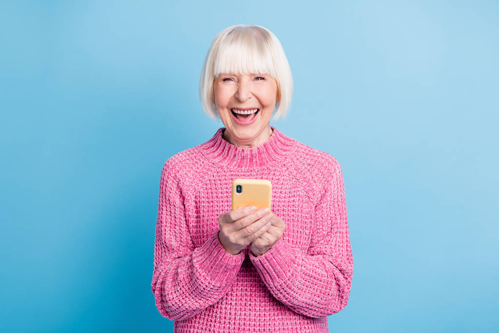 Foto ritratto di eccitata vecchia donna con la bocca aperta che tiene il telefono in due mani isolate su sfondo di colore blu pastello - Foto, immagini