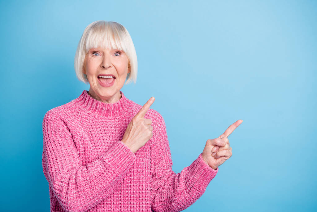 Фотопортрет изумленной кричащей старушки, указывающей двумя пальцами на пустое место, изолированное на пастельно-голубом фоне - Фото, изображение