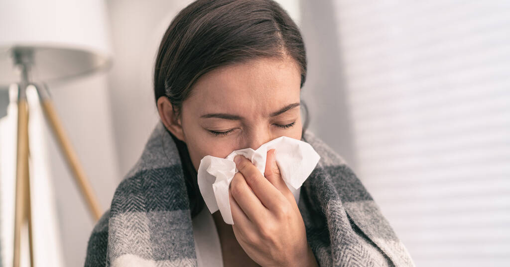 Yskä nenän ja suun peittävässä kudoksessa yskimisen yhteydessä COVID-19-hygieniasuosituksena koronaviruksen leviämisen ehkäisyyn. Aasialainen nainen sairas flunssa kotona - Valokuva, kuva