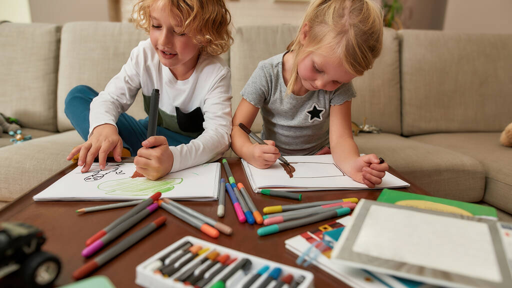 Roztomilý chlapec a dívka malování s markery v obývacím pokoji, zatímco tráví čas spolu doma - Fotografie, Obrázek
