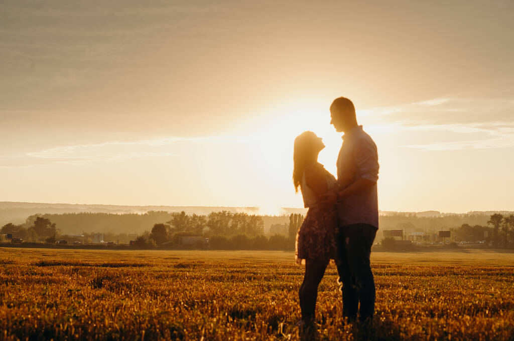 ロマンチックな関係の概念。小麦畑の明るい夕日の中を走っているカップル。秋.  - 写真・画像