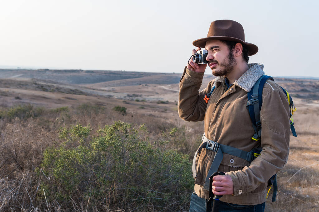 Кавказький турист з бородою, у коричневій куртці, рюкзаку, фотографує поле. - Фото, зображення