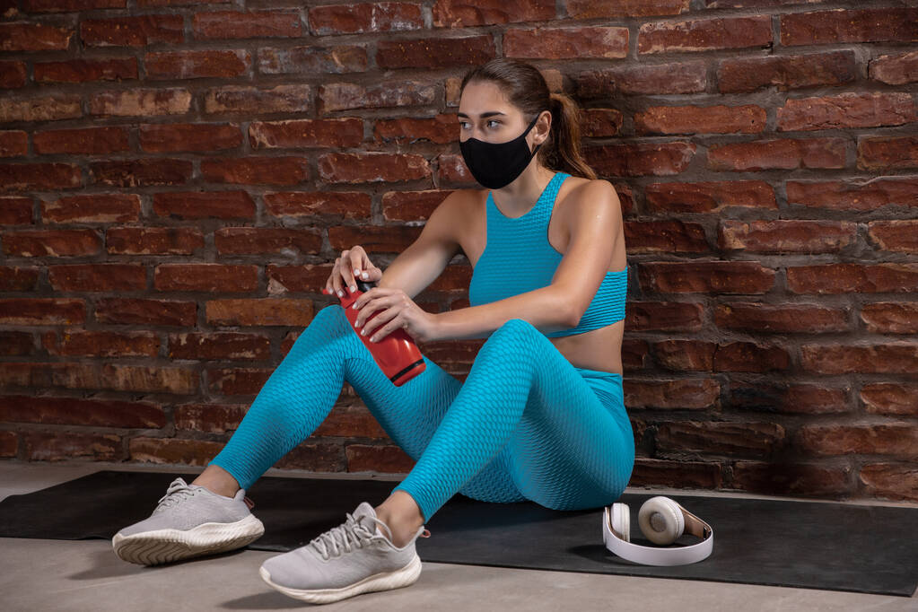Professional female athlete training on brick wall background wearing face mask. Sport during quarantine - Photo, Image