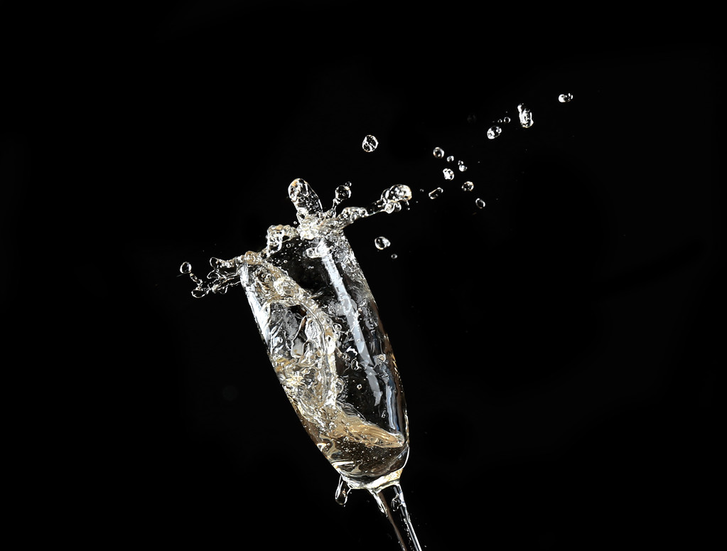 Glass of champagne with splash, on black background - Photo, Image