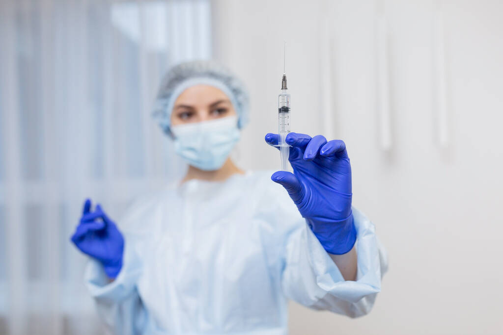 Крупным планом женщины-врача, держащей шприц с инъекцией, молодая женщина-врач в медицинской форме и перчатках держит инъекцию в руках. здоровье и медицинская концепция - Фото, изображение