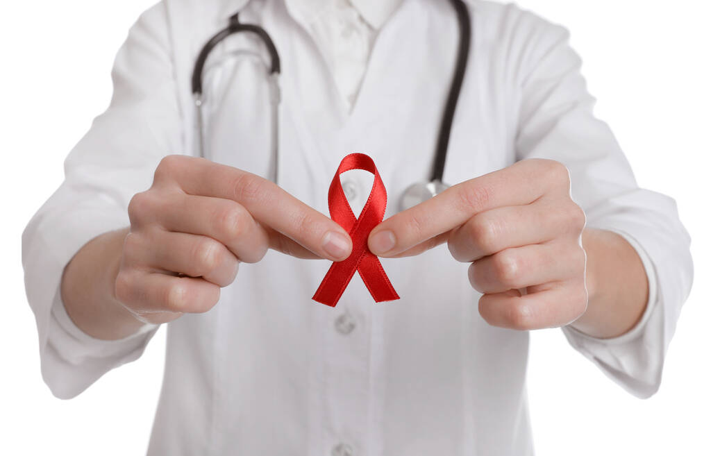 Lekarz trzymający czerwoną wstążkę na białym tle, zbliżenie. Miesiąc świadomości AIDS - Zdjęcie, obraz