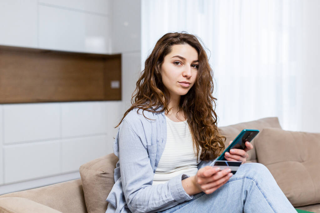 Muotokuva onnellinen nainen shopper käyttäen instant helppo mobiilimaksut tehdä ostoksia verkkokaupassa nuori nainen asiakas tilalla luottokortti ja älypuhelin istuu sohvalla kotona - Valokuva, kuva