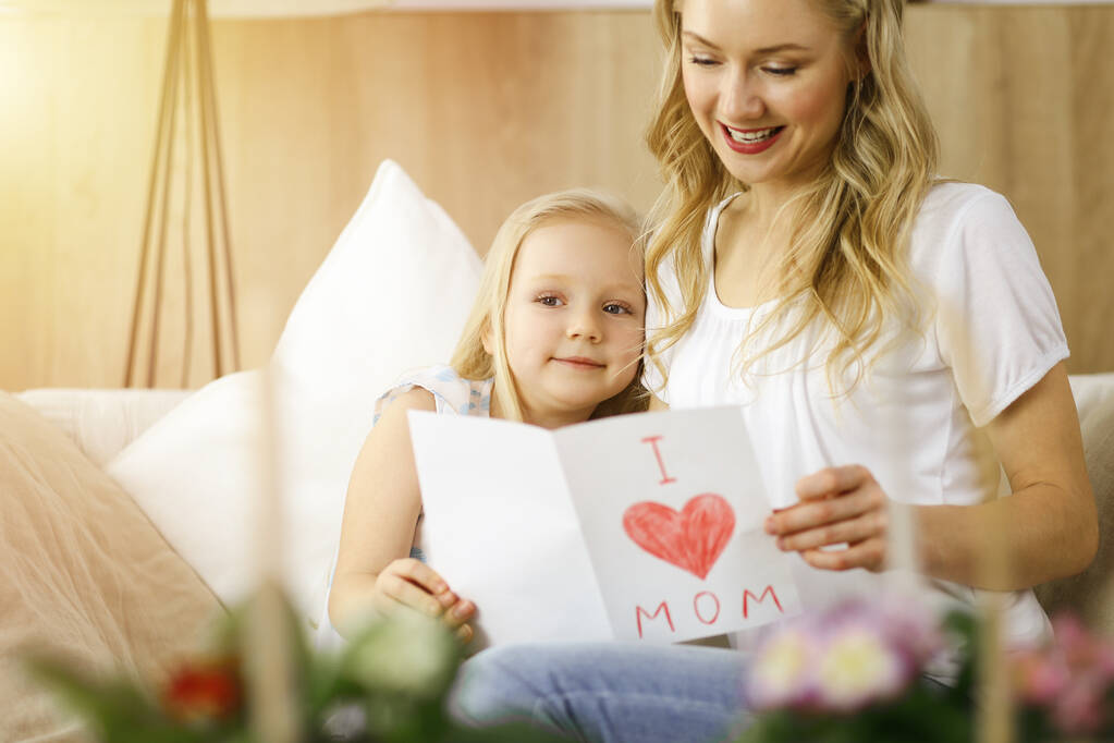 Šťastný den matek ve slunném bytě. Dcera gratuluje mamince a dává jí pohlednici s kresbou srdce. Rodinný koncept - Fotografie, Obrázek