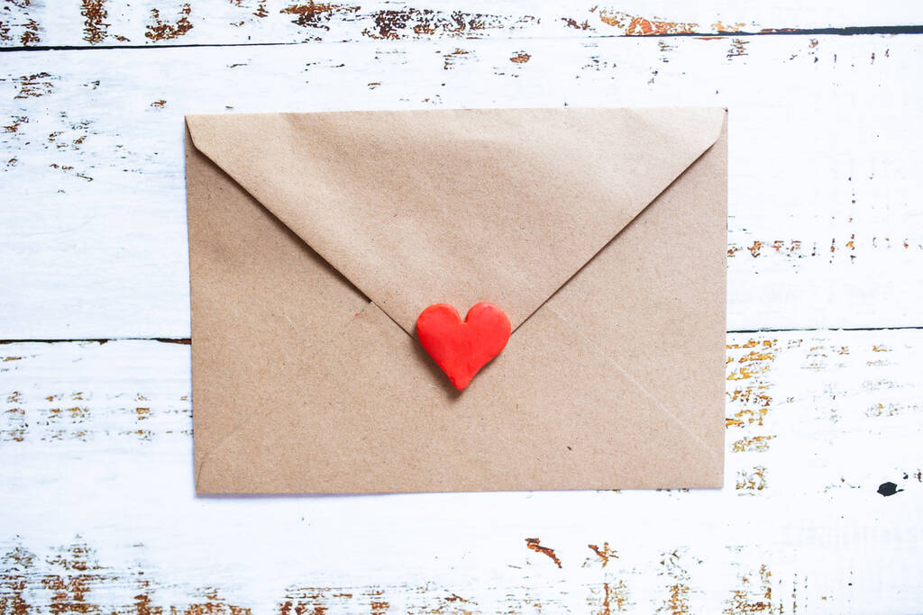 Lettre d'amour dans une enveloppe artisanale avec coeur rouge argile sur fond de bois blanc. - Photo, image