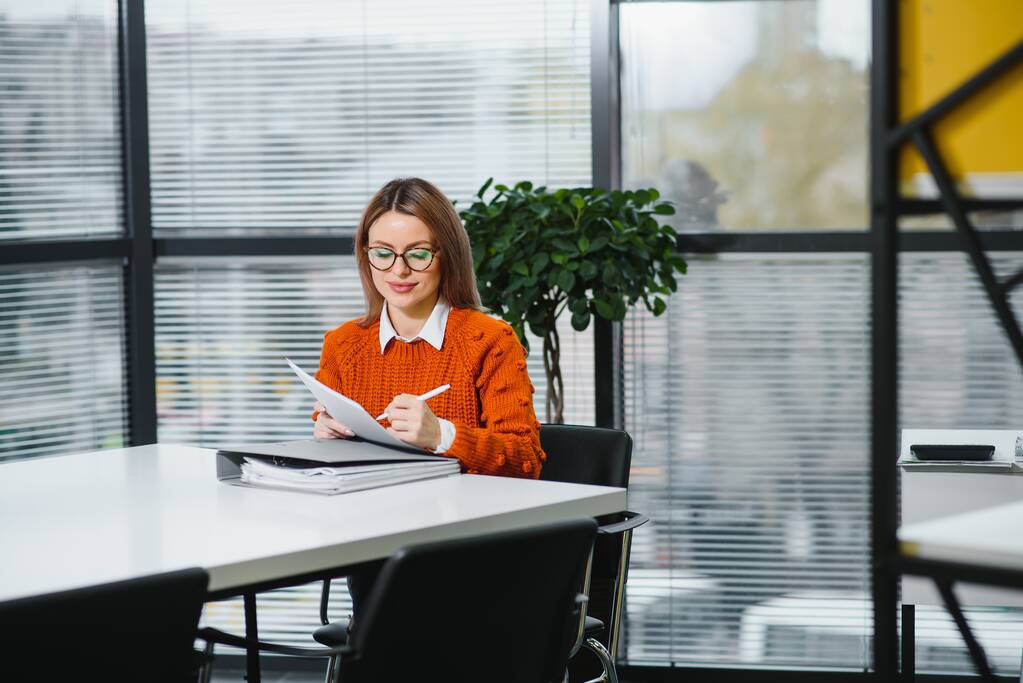 Giovane donna d'affari seduta sul posto di lavoro e carta da lettura in ufficio - Foto, immagini