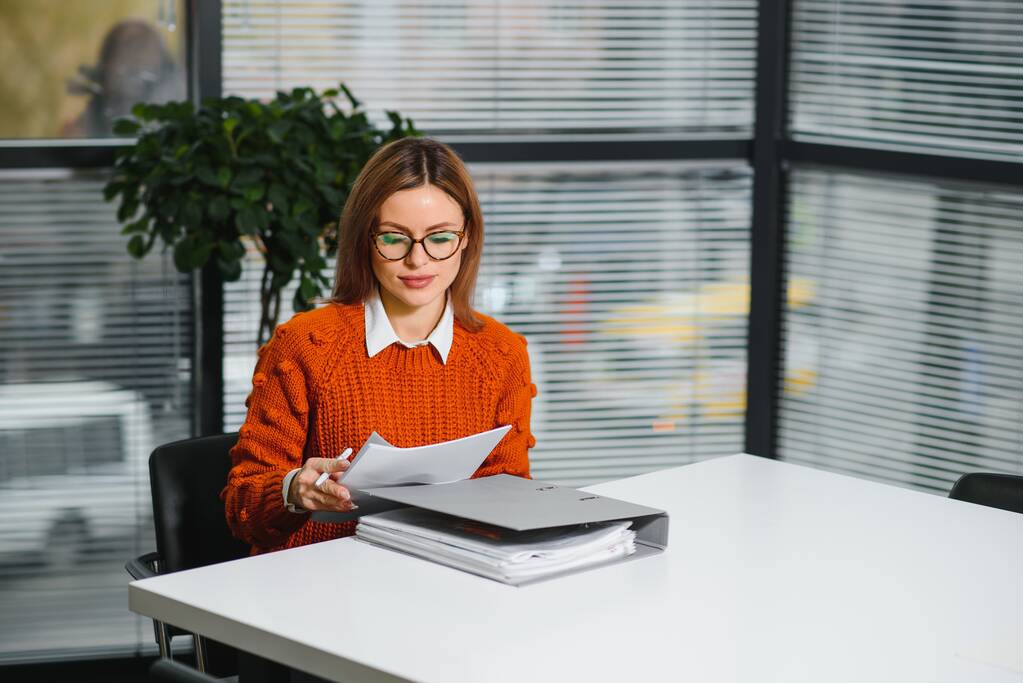 Retrato de una feliz mujer de negocios casual en suéter sentada en su lugar de trabajo en la oficina - Foto, imagen