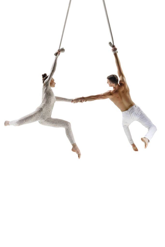 Couple of young acrobats, circus athletes isolated on white studio background. Training perfect balanced in flight - Photo, image