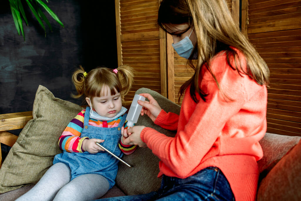 薬局のコンセプト。病気の人は家を出る。子供たちはウイルスから手を治療する。ソファの上の顔のマスクにタブレットと携帯電話で。予防の概念.赤ちゃんは怖がって - 写真・画像