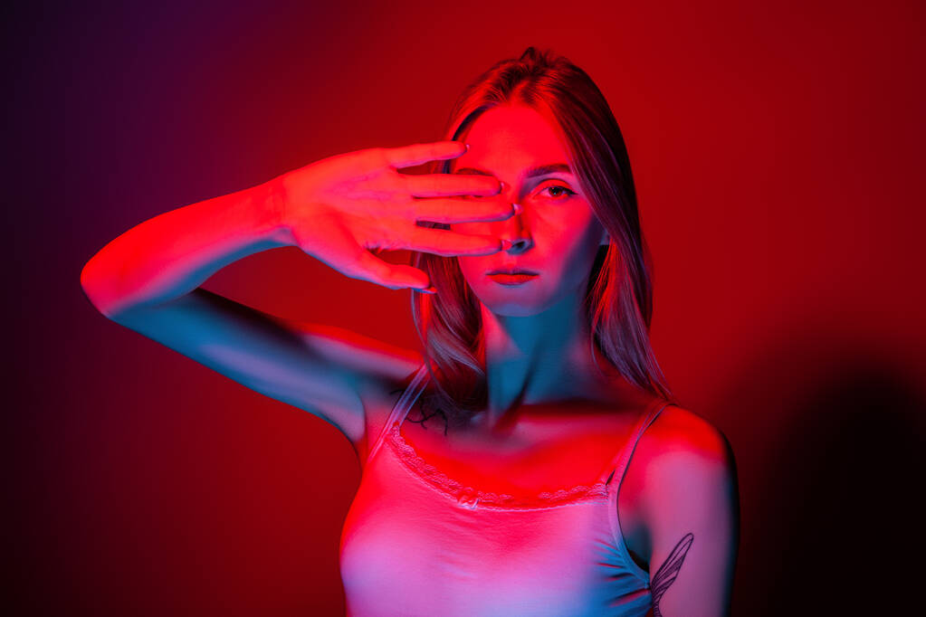 Tunteeton nuori nainen peittää silmät käsin studiossa punaisella valolla - Valokuva, kuva