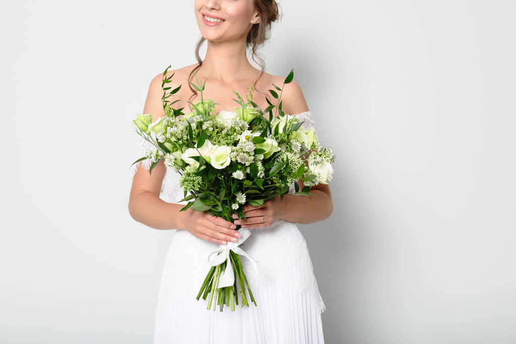 Young bride wearing wedding dress with beautiful bouquet on light grey background, closeup - Photo, Image