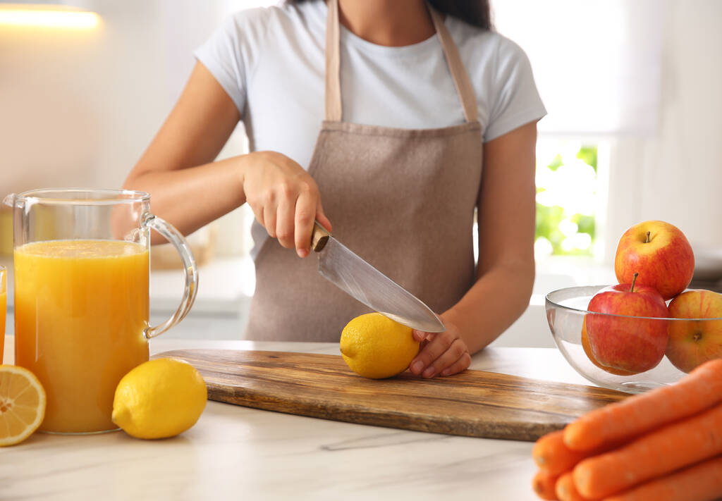 Fiatal nő vágás friss citrom gyümölcslé asztalnál a konyhában, közelkép - Fotó, kép