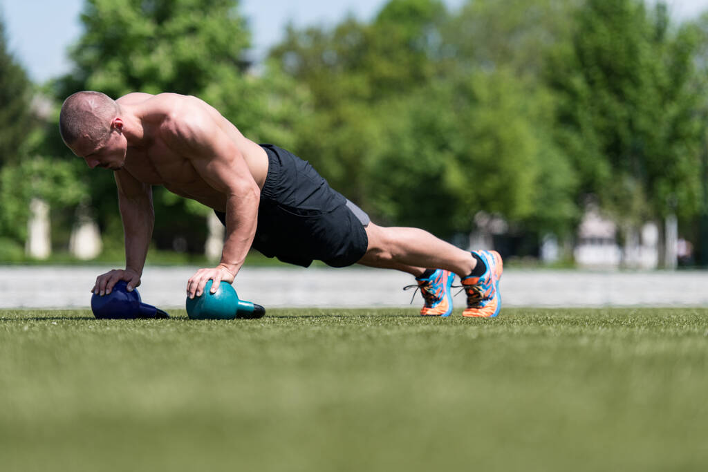 Zdrowy człowiek sportowiec robi pompki Trening z Kettle Bell na zewnątrz - Kettle-bell Ćwiczenia - Zdjęcie, obraz