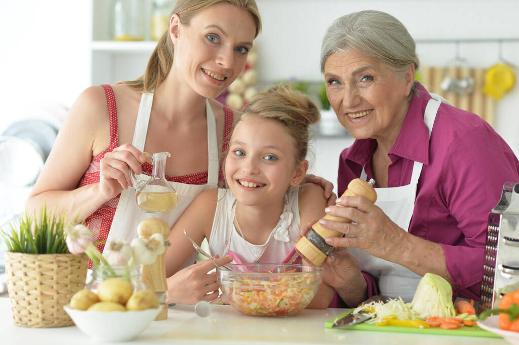 Schattig meisje met moeder en oma bereiden heerlijke verse salade in de keuken - Foto, afbeelding
