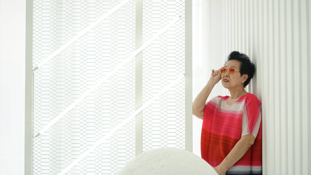 Asiática anciano mujer senior modelo rojo tono vestido y gafas de sol en blanco espacio fondo - Foto, imagen