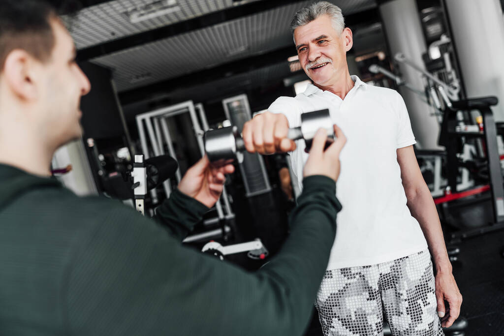 Тренер по фитнесу помогает старшему мужчине в упражнениях. Сосредоточься на старших. Закрыть. - Фото, изображение