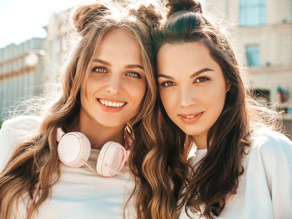 Retrato de dos jóvenes y hermosas mujeres hipster sonrientes en ropa de camisetas blancas de verano de moda.Sexy mujeres despreocupadas posando sobre el fondo de la calle. Modelos positivos que se divierten y abrazan - Foto, Imagen