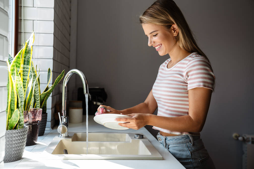 Портрет усміхненої молодої жінки, що миє посуд на кухні
 - Фото, зображення