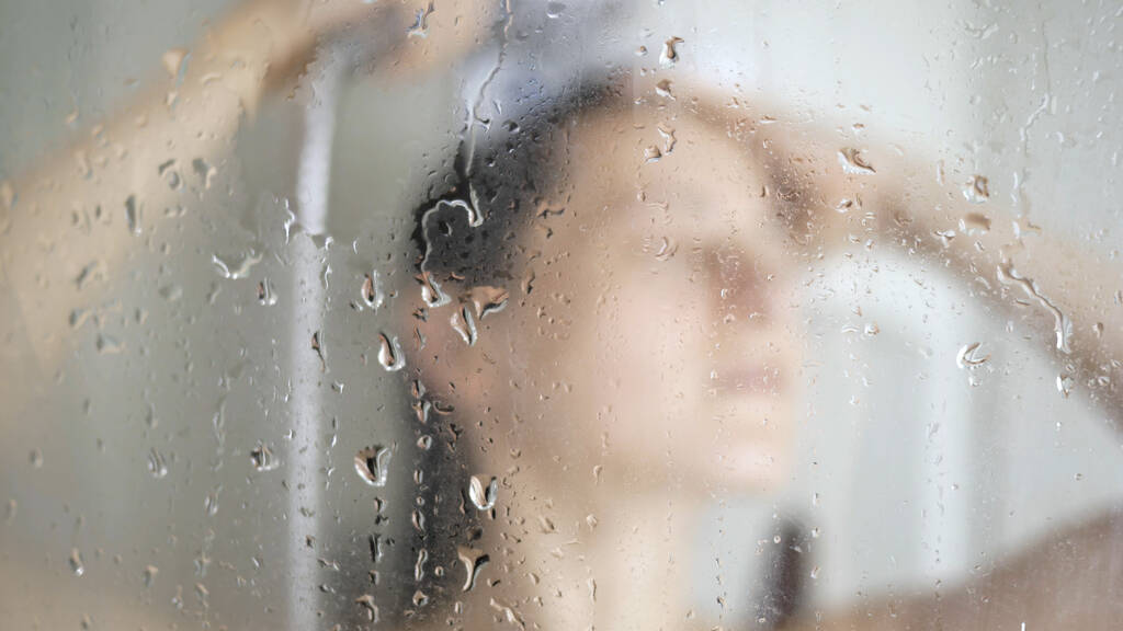 Beautiful girl taking shower behind glass, selective focus on glass drops water. - Photo, Image