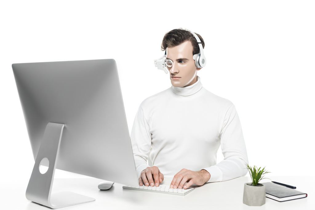 Киборг в глазных линзах и наушниках с помощью компьютера рядом с растением и ноутбука изолированы на белом - Фото, изображение