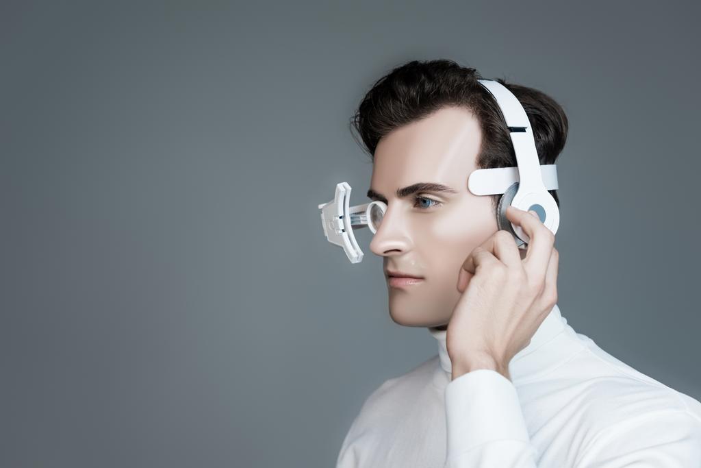 Cyborg mit Augenlinse und Kopfhörer schaut isoliert auf grau - Foto, Bild