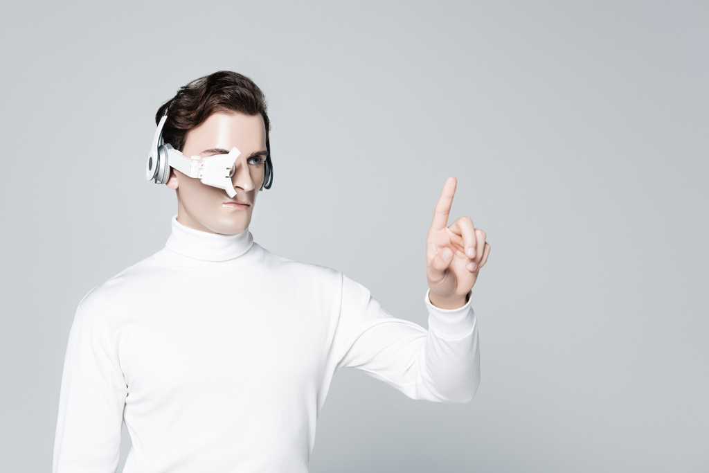 Cyborg mit Kopfhörer und Augenlinse zeigt mit dem Finger isoliert auf grau - Foto, Bild
