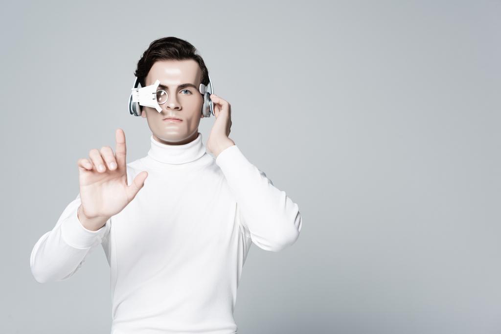 Cyborg com a mão perto de fones de ouvido tocando algo isolado no cinza - Foto, Imagem