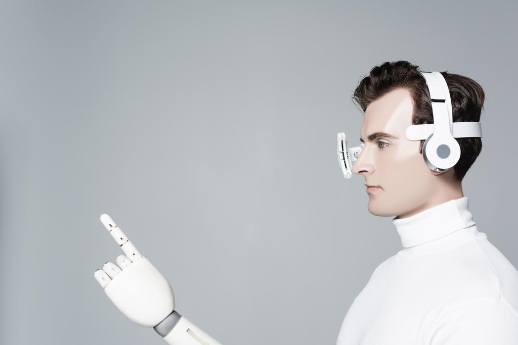 Brunetka cyborg w soczewkach do oczu, słuchawkach i sztucznej dłoni wskazując palcem odizolowanym na szaro - Zdjęcie, obraz