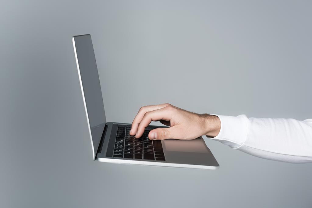 Обрезанный вид человека с помощью ноутбука с чистым экраном в воздухе изолированы на сером - Фото, изображение