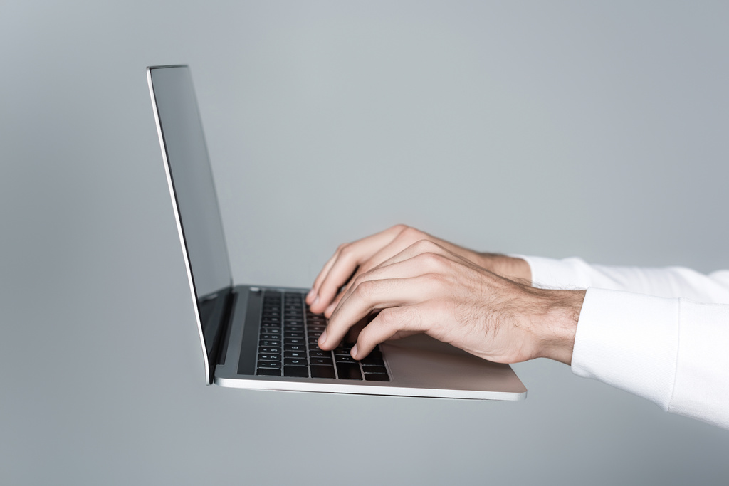 Vista recortada del hombre usando el ordenador portátil aislado en gris - Foto, Imagen