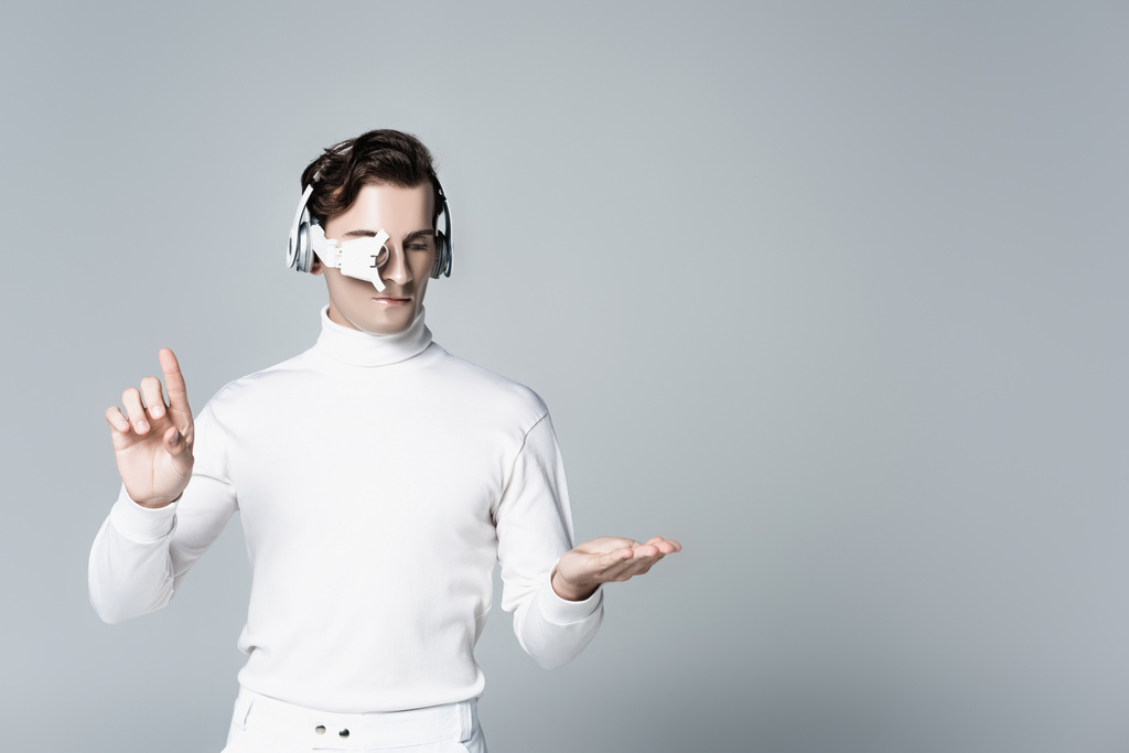Cyborg im Kopfhörer berührt und zeigt auf etwas Isoliertes in Grau - Foto, Bild